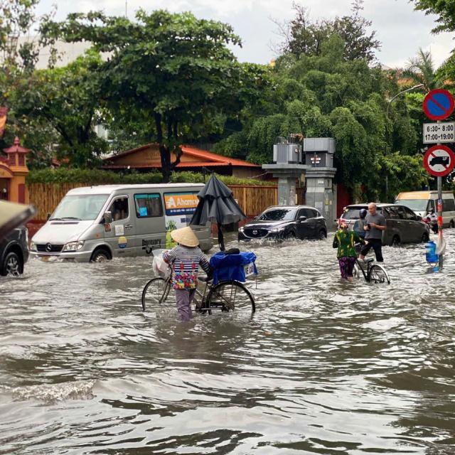 A woman crosses a flooded street with her bicycle in Vietnam