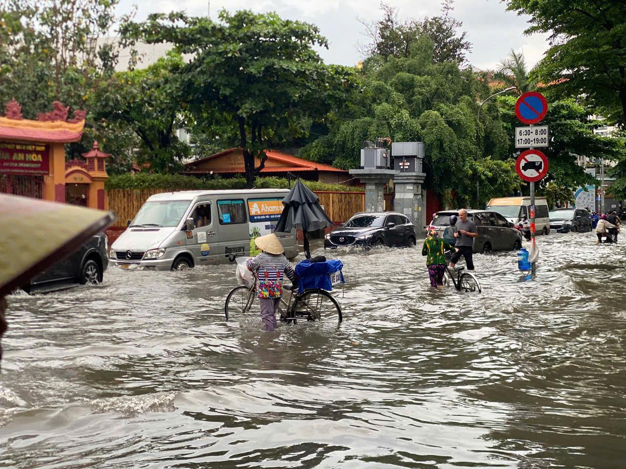 A woman crosses a flooded street with her bicycle in Vietnam